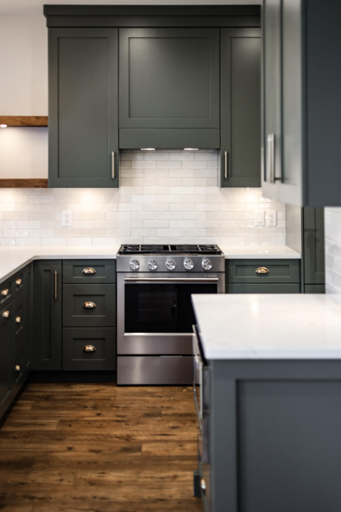 A kitchen with modern grey-green cabinetry, stylish silver hardware and clean white counters and backsplash